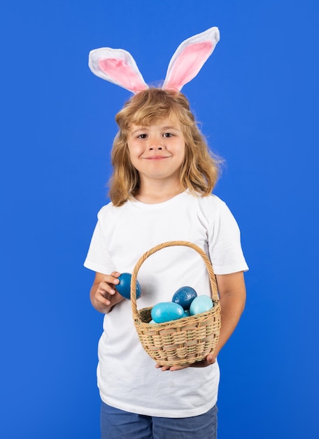 Portret van grappige jongen met bunny oren houden paasmandje met paaseieren geïsoleerd op blauwe studio achtergrond Pasen vakantie konijntjesjacht