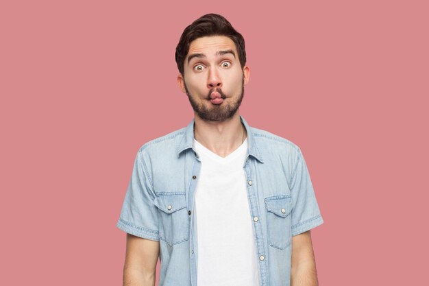 Portret van grappige komische gezicht knappe bebaarde jonge man in blauwe casual stijl shirt permanent met vis lippen en camera kijken. indoor studio opname, geïsoleerd op roze achtergrond.