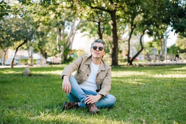 Portret van grijsharige man met zonnebril in een park zittend op het gras kijkend naar de camera