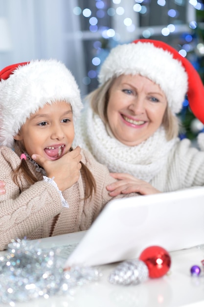 Portret van grootmoeder en haar kleindochter die thuis met Kerstmis laptop gebruiken