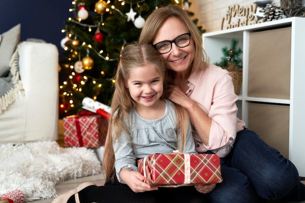 Portret van grootmoeder en kleindochter die elkaar omhelzen naast een kerstboom