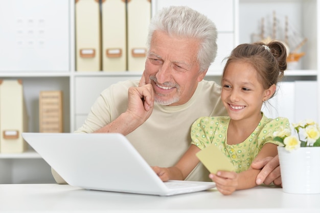 Portret van grootvader en kleindochter die samen laptop gebruiken