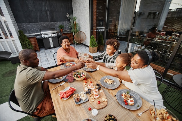 Portret van grote Afro-Amerikaanse familie rammelende glazen terwijl ze samen genieten van een diner in de buitenlucht en ...
