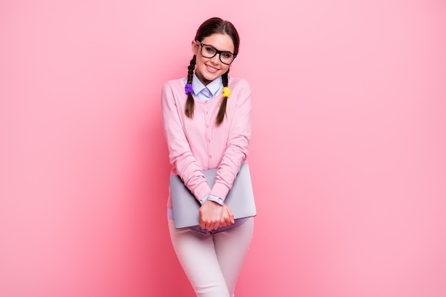 Portret van haar mooie, vrolijke, vrolijke, bescheiden bruinharige tienermeisje die in de hand houdt met behulp van een laptop die leeronderwerp op afstand leert geïsoleerd op een roze pastelkleurige achtergrond