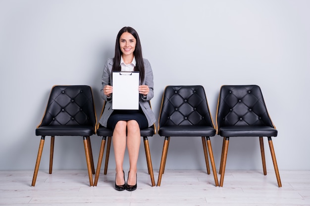 Portret van haar, mooie, vrolijke, zelfverzekerde, succesvolle dame, uitvoerend manager zittend in een stoel met documentverzekering, contact opnemen met klantenondersteuning, geïsoleerde pastelgrijze achtergrondkleur