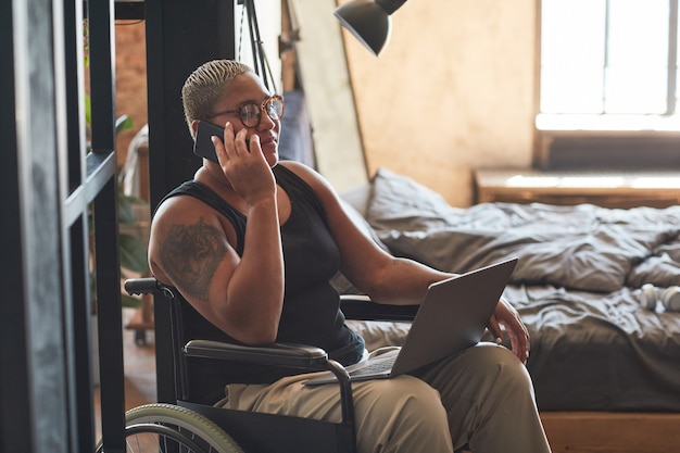 Portret van hedendaagse getatoeëerde vrouw met een handicap die via smartphone spreekt terwijl ze thuis werkt