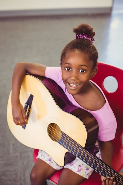 Portret van het glimlachen schoolmeisje het spelen gitaar in klaslokaal