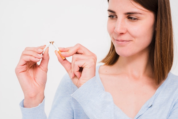 Foto portret van het glimlachen van vrouwen brekende sigaret over witte muur