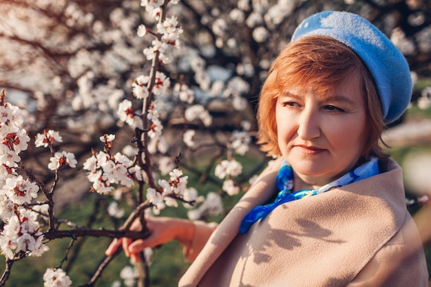 Portret van het hogere vrouw ontspannen in de lentetuin in abrikozenbloesem die de lenteaard bewonderen