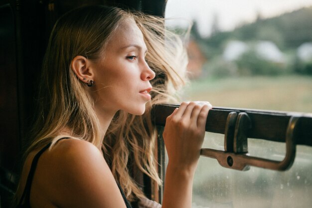 Portret van het jonge mooie blonde haarmeisje kijken uit venster van het berijden van trein