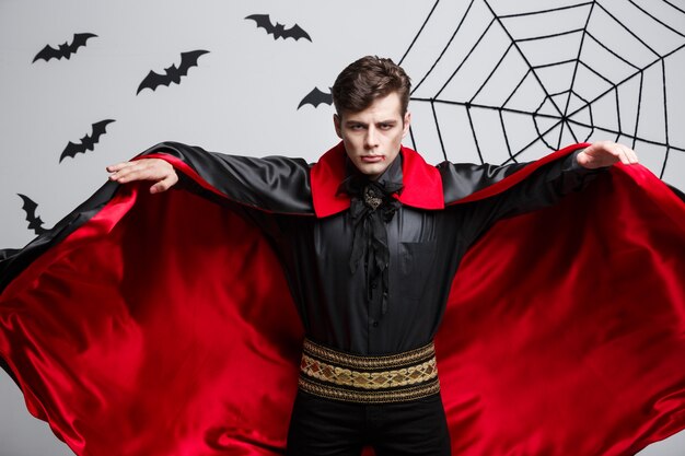 Portret van het knappe Kaukasische kostuum die van Halloween van de Vampier zijn rode, zwarte mantel fladderen.