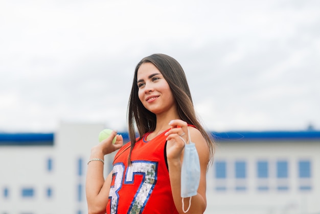 Portret van het meisje dat van de tennisspeler een bal buiten met beschermende maskers houdt