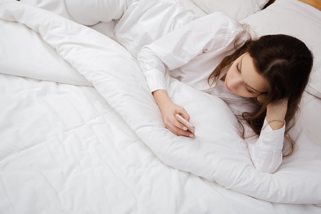 Portret van het meisje liggend op bed met mobiele telefoon