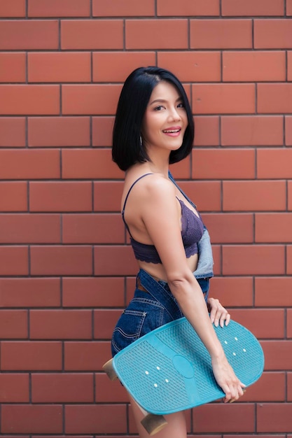 Portret van hipster meisje met skateboard op bakstenen muur achtergrond Mooie Aziatische vrouw poseren voor het nemen van een foto