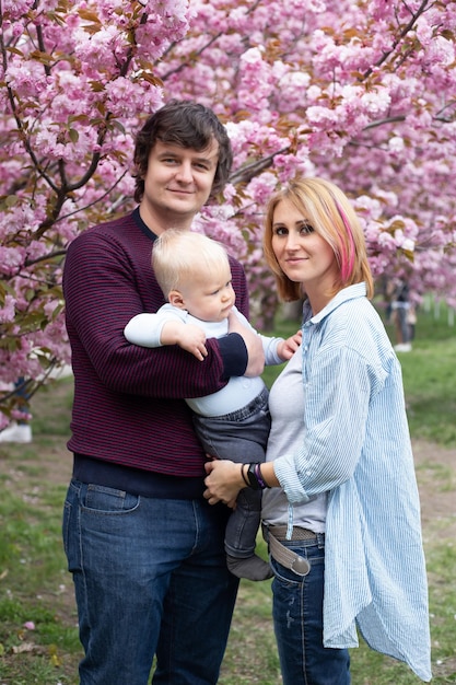 Portret van hipster-ouders met hun zoon in het voorjaar in de buurt van de Japanse kersensakura ontmoeten de lente Sakura bloeit heel mooi met roze bloemen