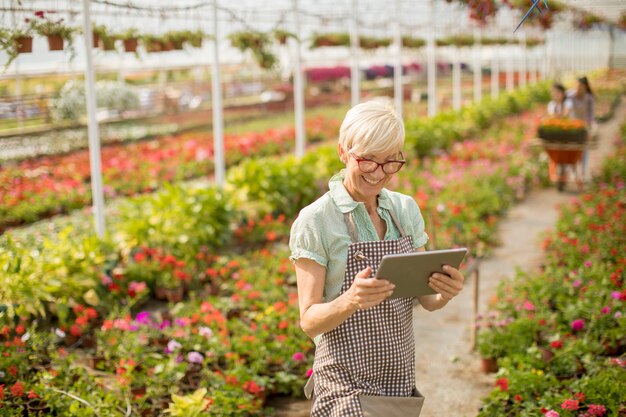 Portret van hogere vrouw die tablet in bloemtuin gebruiken