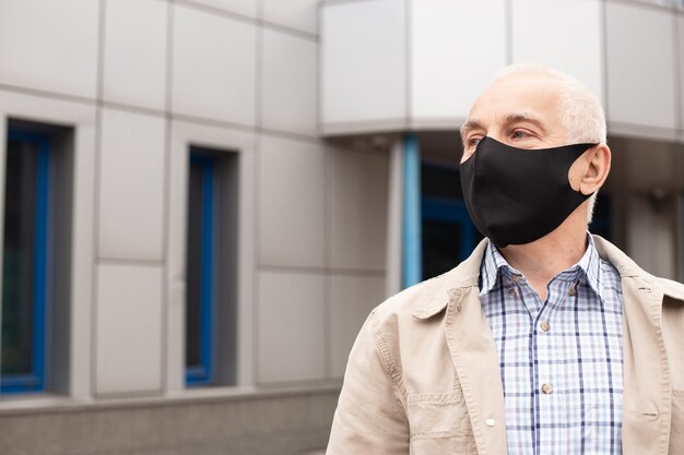 Portret van hogere zakenman die protecitve-masker in stad dichtbij bureaugebouwen dragen