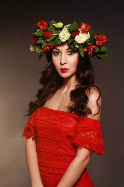 Portret van ideale vrouw met een krans van bloemen op haar hoofd en rode jurk.