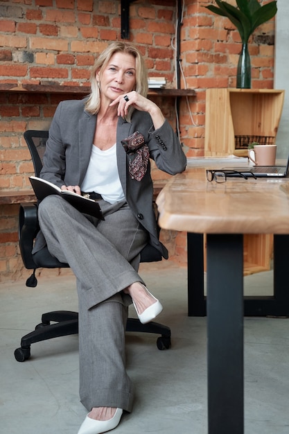 Portret van inhoud volwassen zakelijke dame in stijlvol pak notities in de organisator bekijken tijdens het plannen van taken