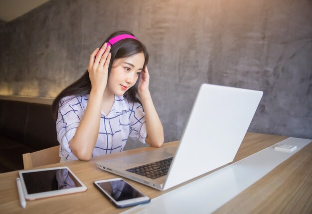 Portret van Jong Aziatisch geluk die hoofdtelefoons dragen die laptop computer thuis voor het werken gebruiken