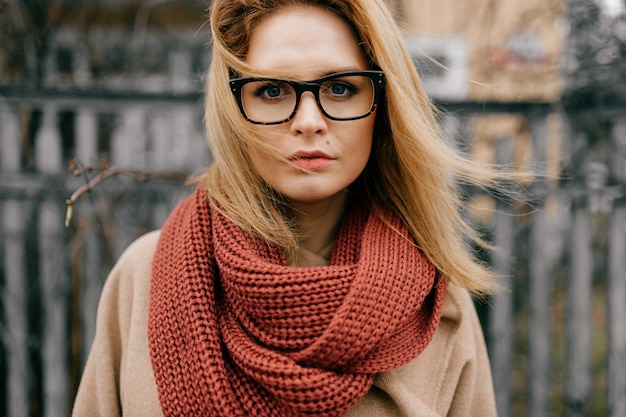 Portret van jong elegant blond meisje met glazen en sjaal die in openlucht stellen