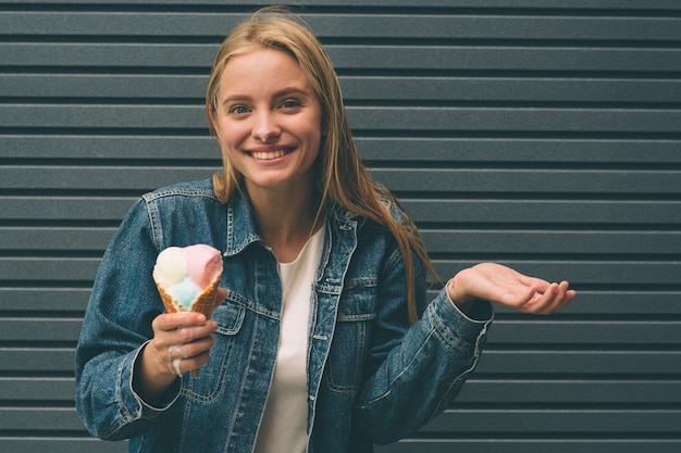 Portret van jong gelukkig meisje dat roomijs over blauwe muurachtergrond eet