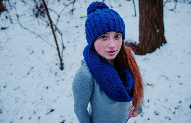 Portret van jong rood haarmeisje met sproeten die bij blauwe gebreide wollen hoed en sjaal in de winterdag dragen.