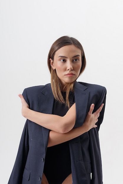 Portret van jonge aantrekkelijke Aziatische vrouw met lang haar in zwarte bodysuit en blauw kostuum dat op witte studioachtergrond wordt geïsoleerd. magere mooie vrouw poseren op cyclorama. modelproeven van mooie dame