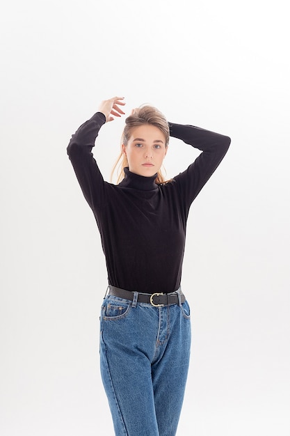 Portret van jonge aantrekkelijke blanke vrouw met lang haar in zwarte coltrui, spijkerbroek geïsoleerd op een witte studio achtergrond. magere mooie vrouw die zich voordeed op cyclorama. modeltests van mooie dame