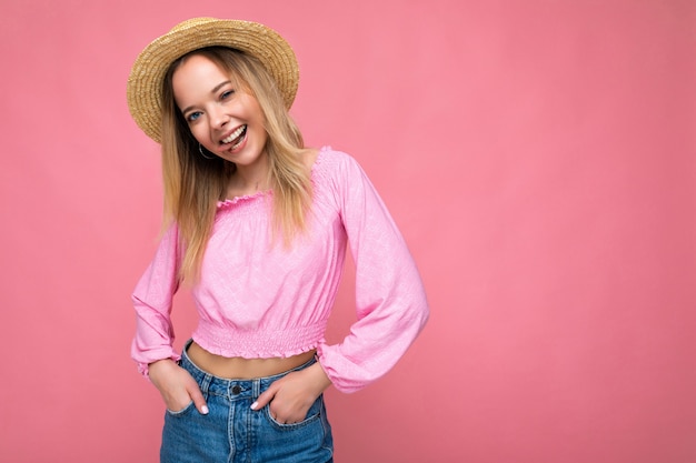 Portret van jonge aantrekkelijke glimlachende hipster blonde vrouw in stijlvolle roze crop top en strohoed