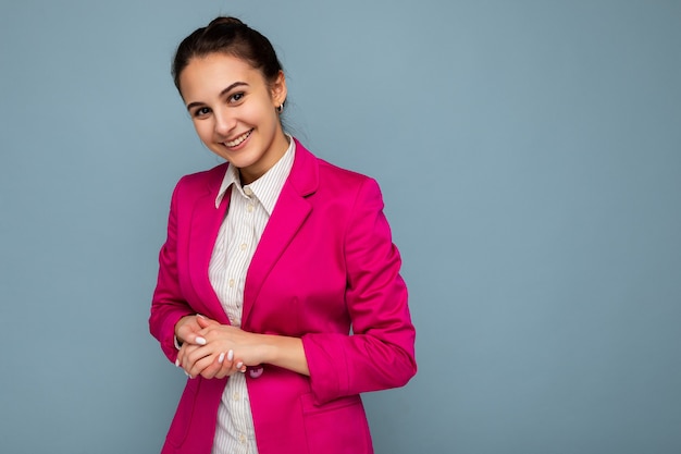 Portret van jonge aantrekkelijke mooie positieve glimlachende brunette vrouw met oprechte emoties, gekleed in casual wit overhemd en trendy roze jasje geïsoleerd dan blauw