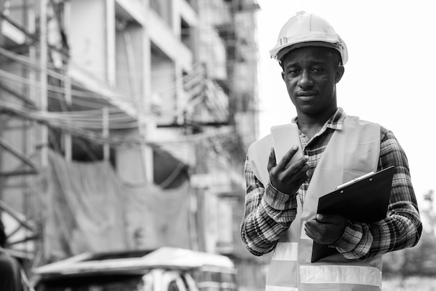 Portret van jonge Afrikaanse man bouwvakker op de bouwplaats buiten in zwart-wit