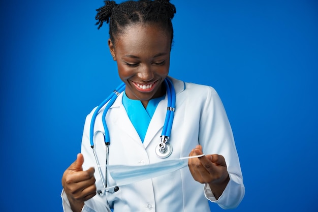 Portret van jonge afrikaanse vrouwelijke arts met medisch masker in blauwe studio