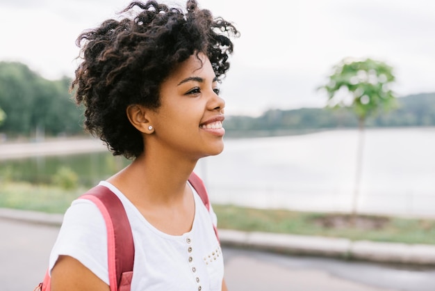 Portret van jonge Afro-Amerikaanse student vrouwelijke glimlachend en klaar om te gaan naar de universiteit wandelen in het park mooie afro tiener vrouw met rugzak poseren buiten mensen en onderwijs