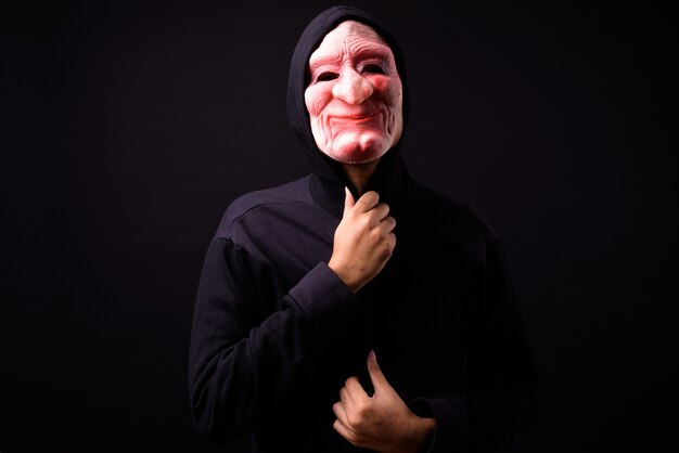 portret van jonge Aziatische man met hoodie en horror masker op zwart