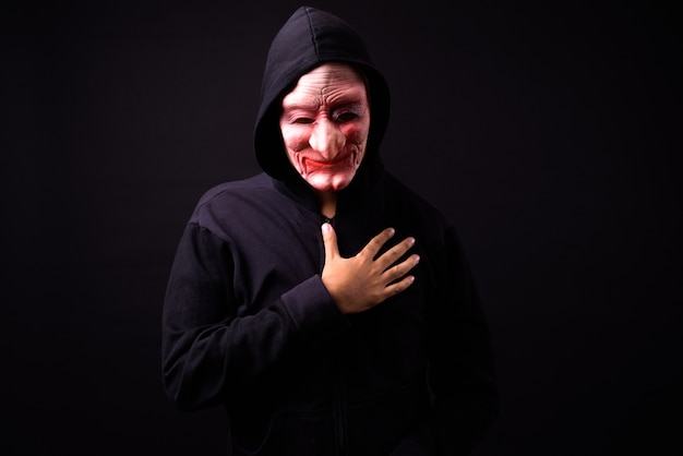 portret van jonge Aziatische man met hoodie en horror masker op zwart