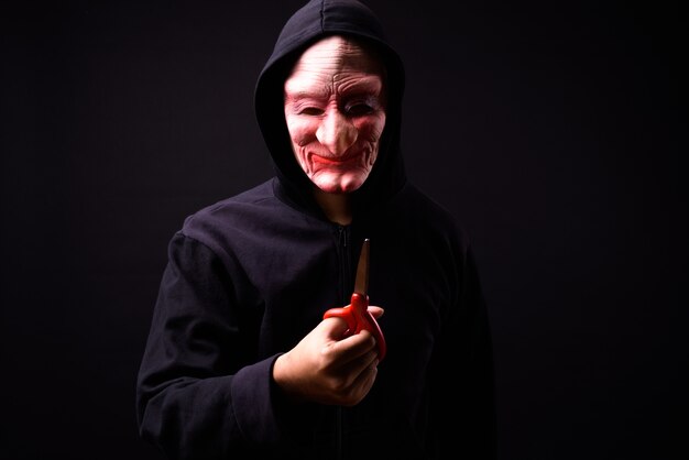 portret van jonge Aziatische man met hoodie en horror masker op zwart