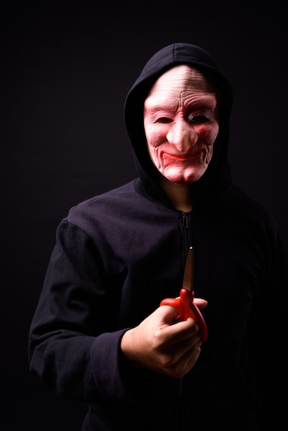 portret van jonge Aziatische man met hoodie en horror masker op zwart