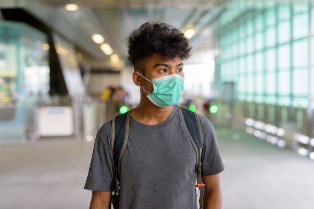 Portret van jonge aziatische toeristenmens als backpacker met masker voor bescherming tegen uitbraak van coronavirus op het skytrain-station