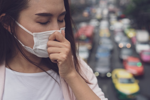 Portret van jonge aziatische vrouw die medisch gezichtsmasker in de stadsstraat draagt.