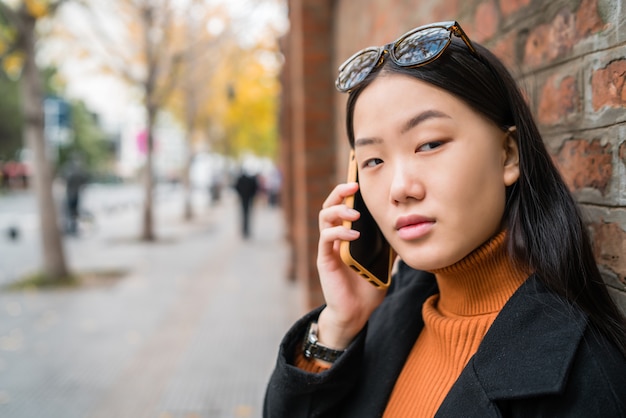 Portret van jonge Aziatische vrouw praten aan de telefoon buiten in de straat.