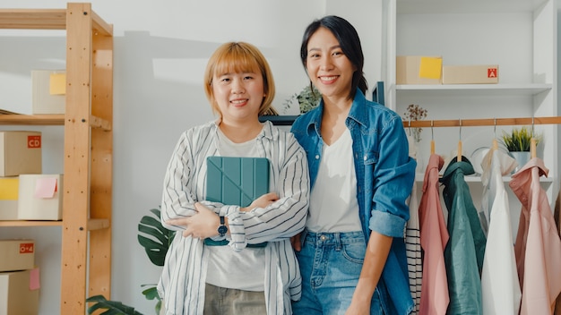 Portret van jonge aziatische vrouwen modeontwerper met gelukkige glimlach, gekruiste armen en kijken naar de voorkant tijdens het werken in kledingwinkel in kantoor aan huis