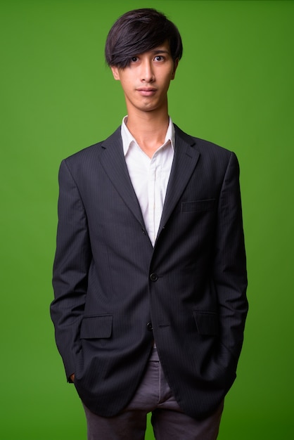 Portret van jonge Aziatische zakenman tegen groene muur
