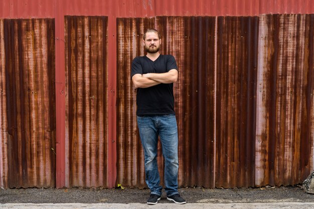 Portret van jonge bebaarde man tegen oude roestige plaat muur