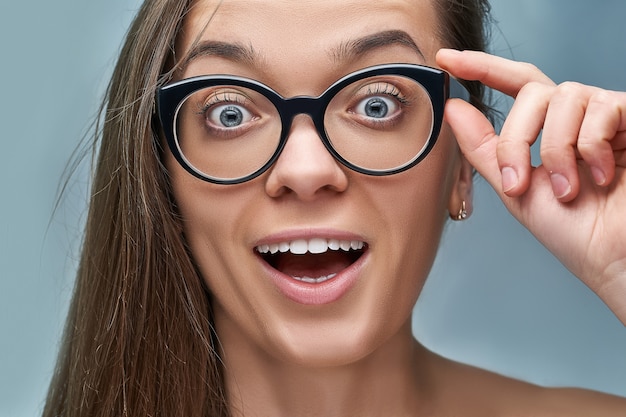 Portret van jonge blanke vrouw met verbaasd opgewonden opgewonden geschokt gezichtsuitdrukking in zwart frame glazen met open mond in verrassing en wijd open ogen. wauw en omg