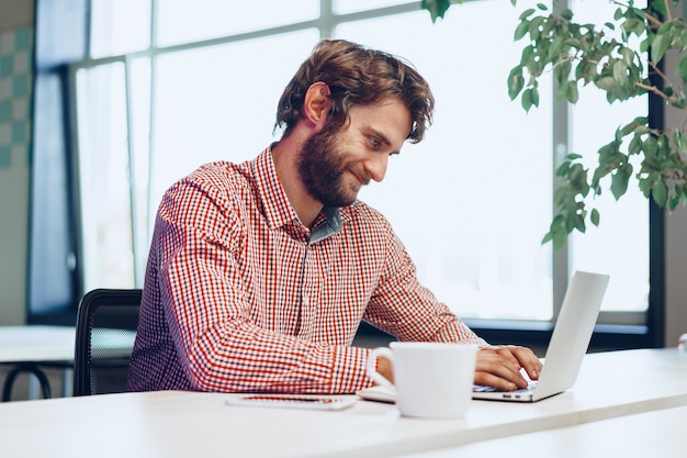 Portret van jonge blanke zakenman met laptopcomputer op zijn werkplek in moderne kantoren