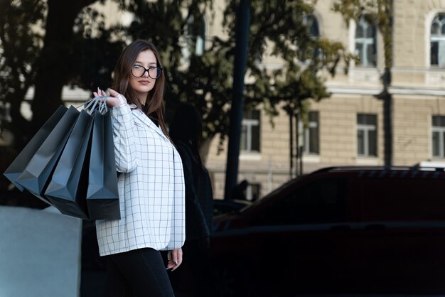 Portret van jonge brunette meisje met boodschappentassen. Mooi meisje in de buurt van een modewinkel. Black Friday winkelen.