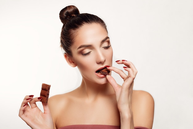 Portret van jonge donkerbruine vrouw die chocolade eet