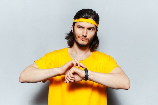 Portret van jonge doordachte en zelfverzekerde man in geel overhemd, met behulp van smartwatch