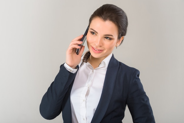 Portret van jonge ernstige vrouw in zakelijke outfit praten aan de telefoon op de grijze achtergrond